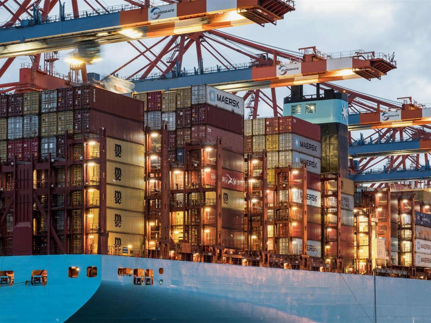 Containers stacked and lit alongside a cargo vessel during night loading operations