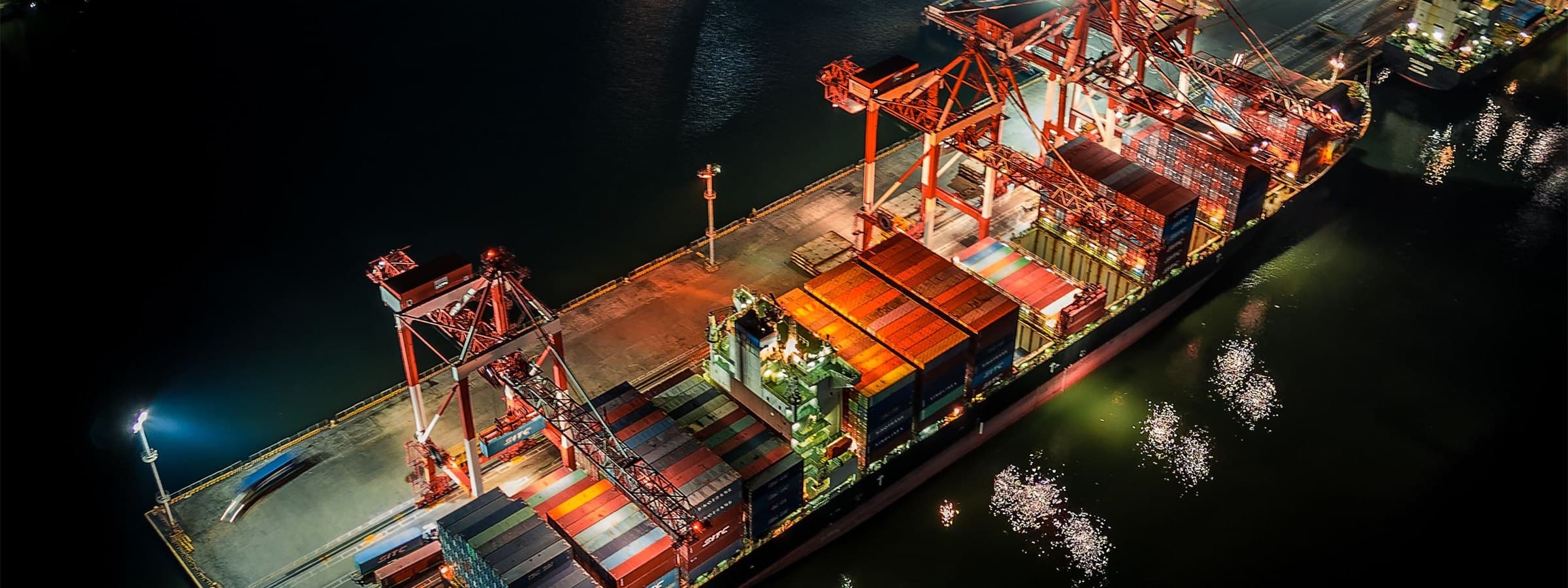 A container vessel being loaded alongside a lit terminal, seen from above